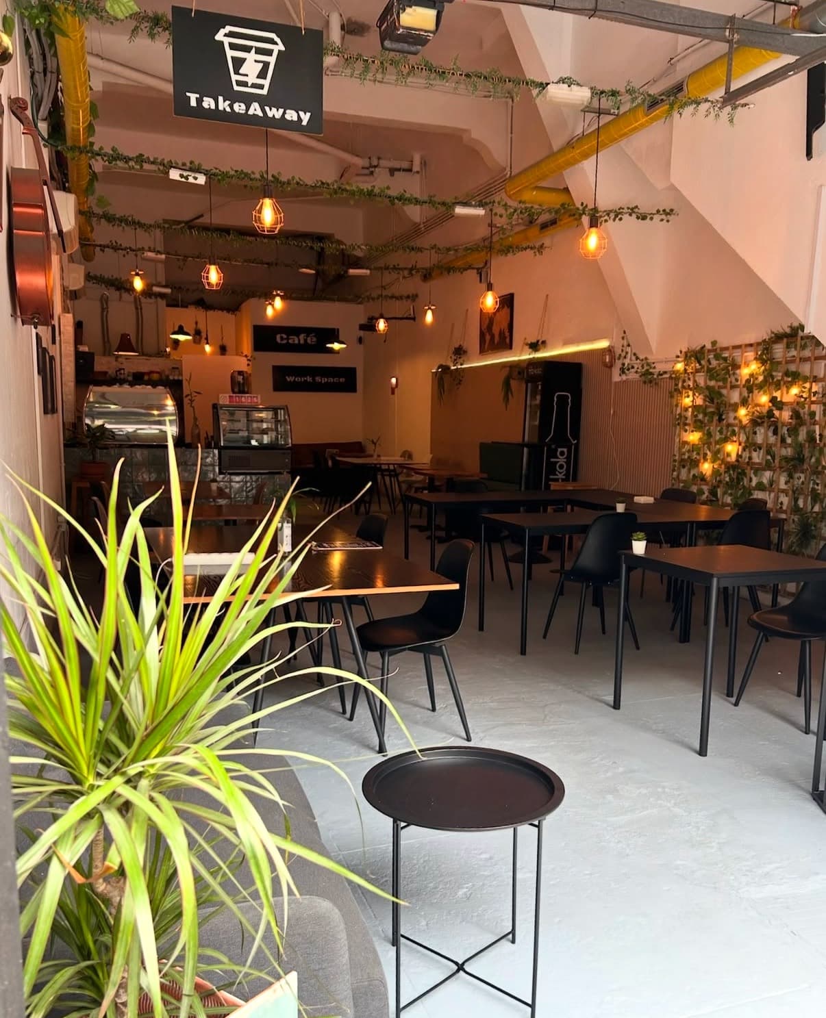 Interior del café: plantas, bombillas colgantes y mesas preparadas.